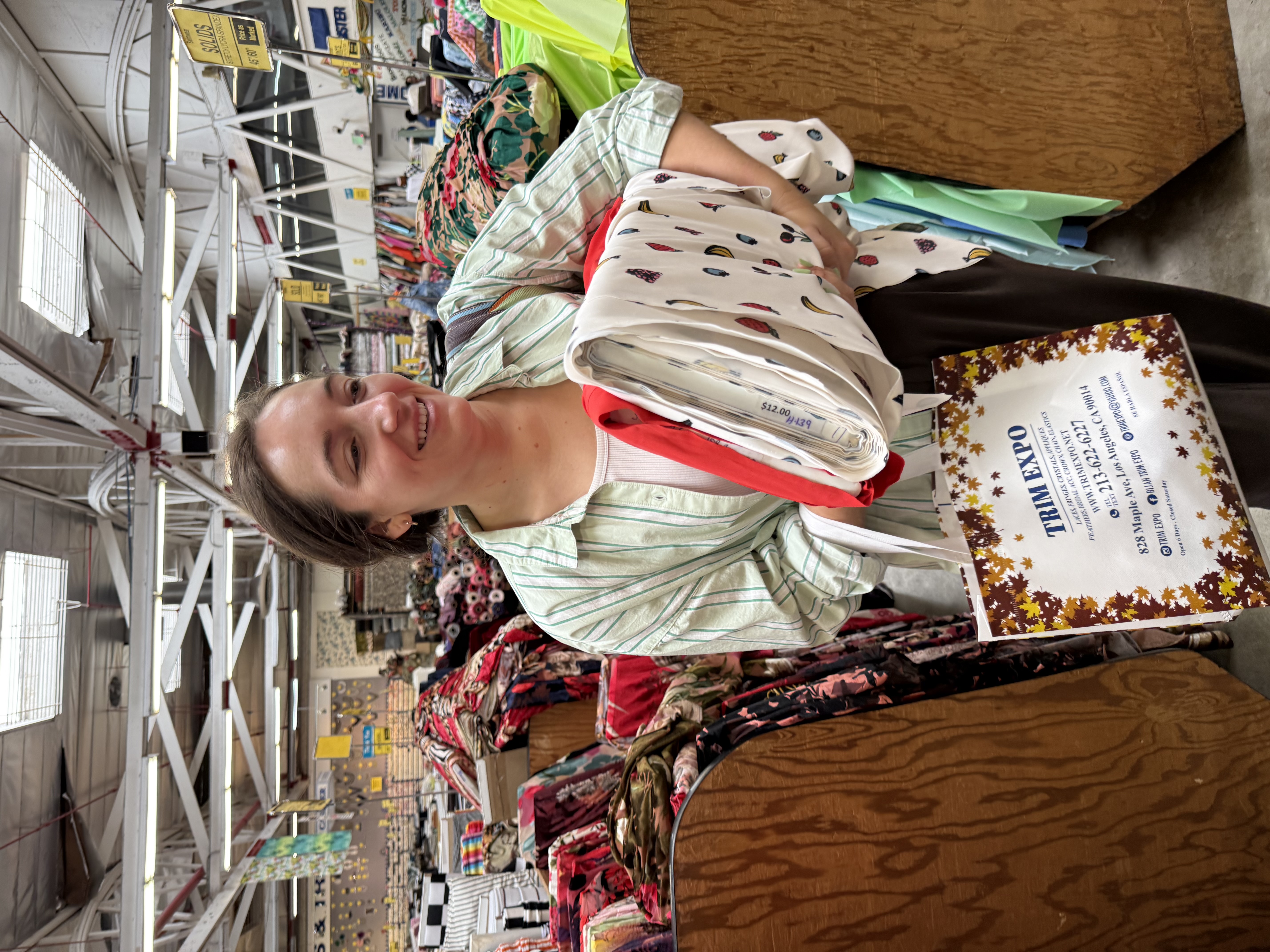 Emily holding the white fruit print fabric and red lining fabric she picked out at Trim Expo